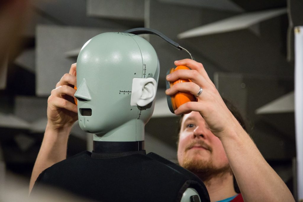 A reseracher placing hearing protectors on acoustic HATS