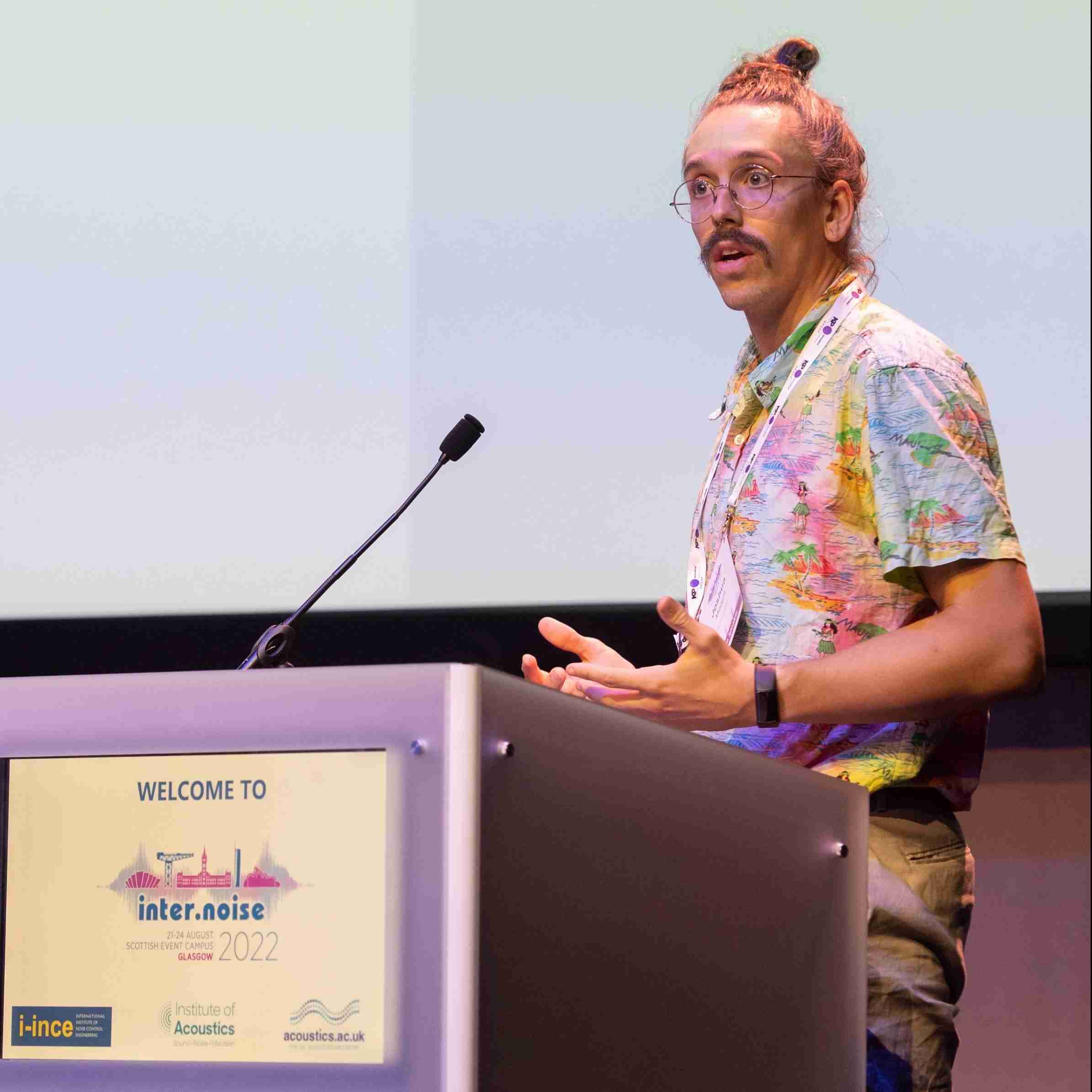 Picture of Dr. Joshua Meggitt speaking at a lectern.