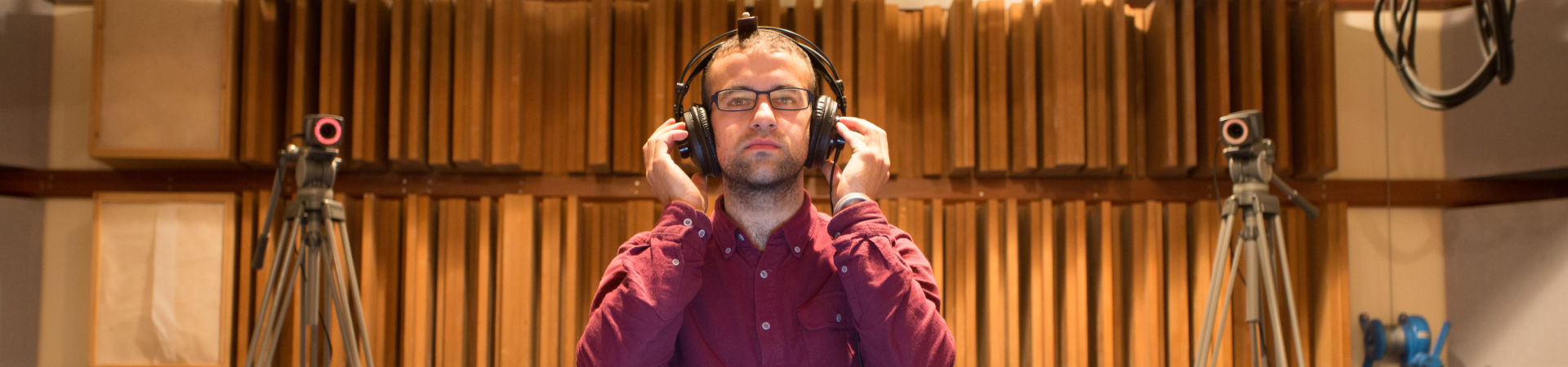 A photograph of a man, sat inside a listening room, wearing headphones.